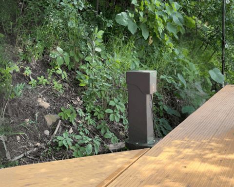 A Pedoc power pedestal with a side mounting bracket installed dockside. The pedestal has a sleek, durable design, providing reliable outdoor power access for marine or dock applications.